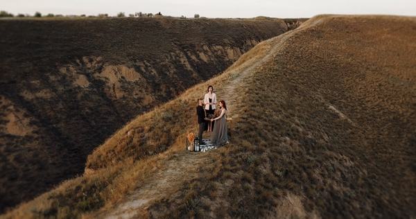 three people standing on a hillside during sunset with a dog surrounded by grass