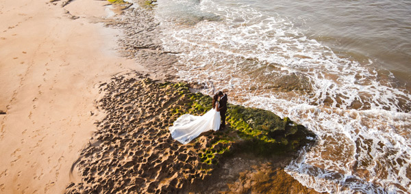 couple embracing on rocky beach with wedding attire and ocean waves in background romantic moments wedding photography coastal scenery