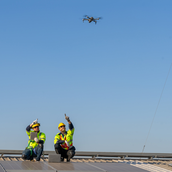 two construction workers on a rooftop pointing at a drone flying above while working on solar panels three innovative technologies in action