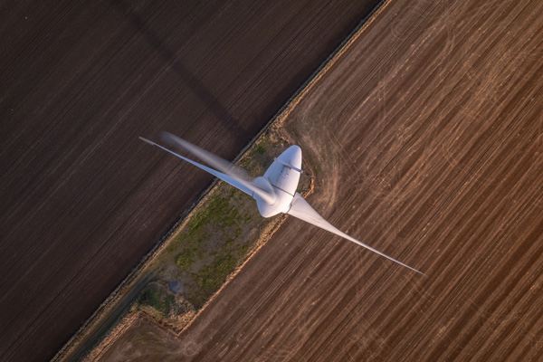 aerial view of a wind turbine above farmland with brown and green fields renewable energy wind power technology